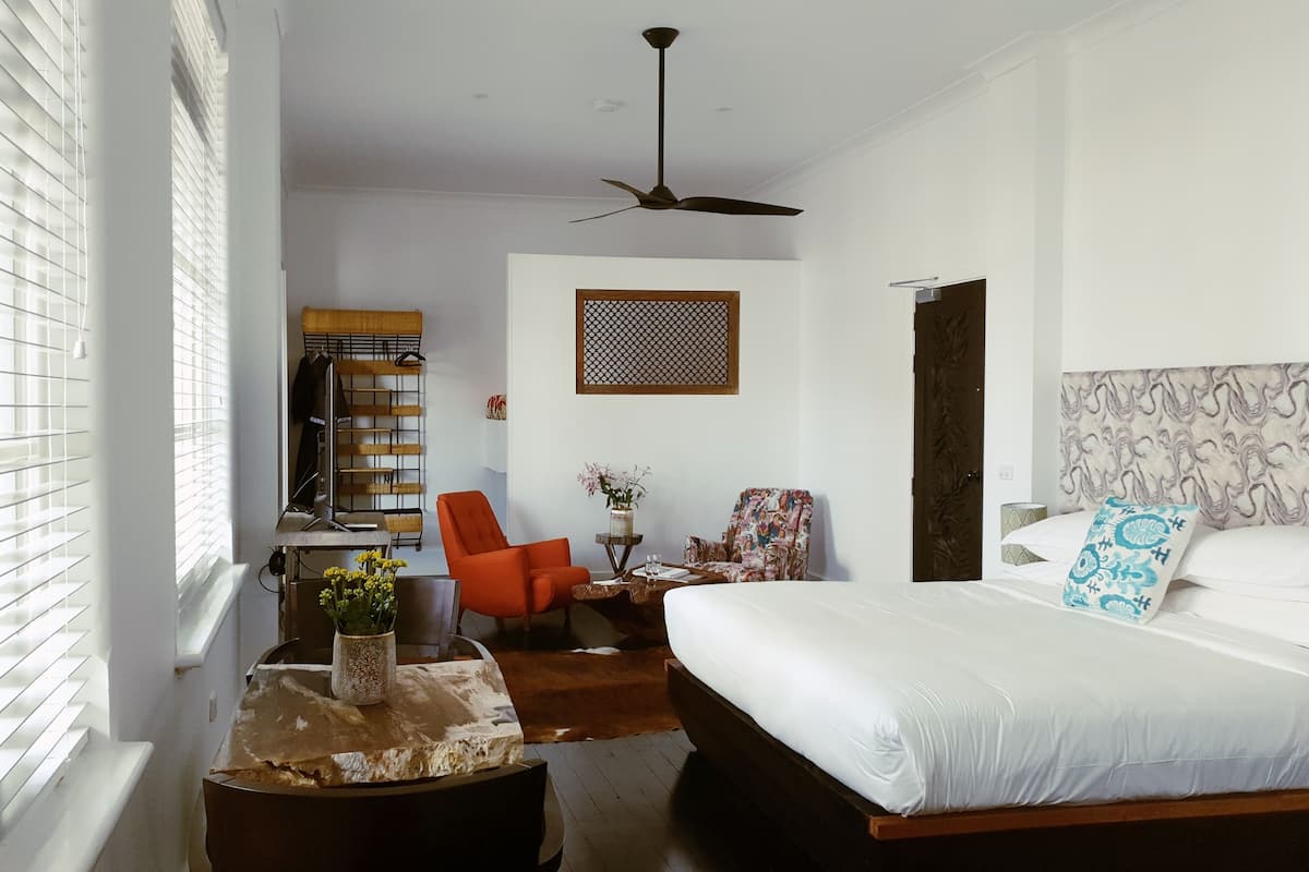 A bedroom with a bed, a desk, a chair, and a window with blinds.