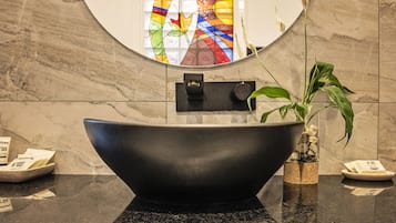 Une salle de bain moderne avec un grand lavabo foncé, une plante en pot et un vitrail en arrière-plan.
