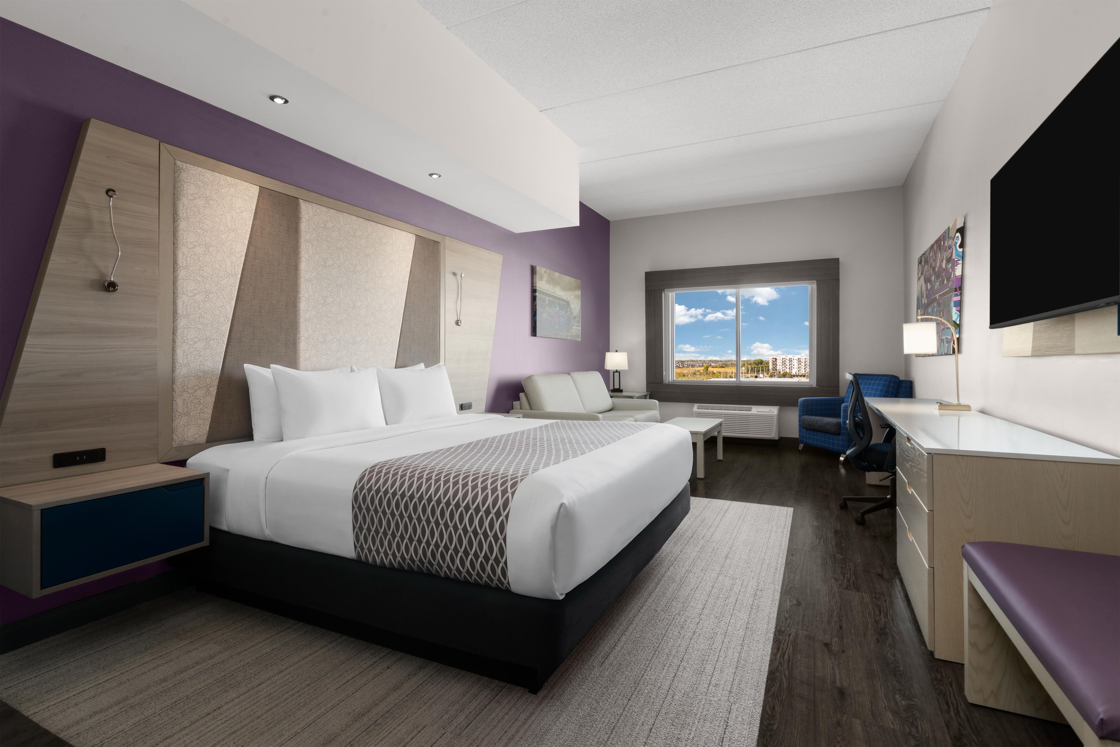 A modern hotel room with a large bed, a desk, a chair, a TV, and a window with a city view.