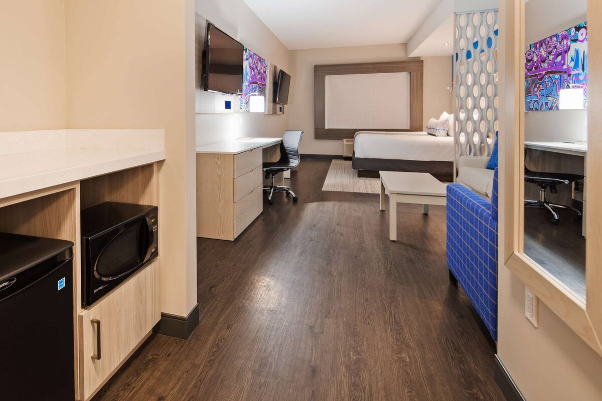Ein kleines Hotelzimmer mit Kochnische, Bett, Schreibtisch und Fernseher.