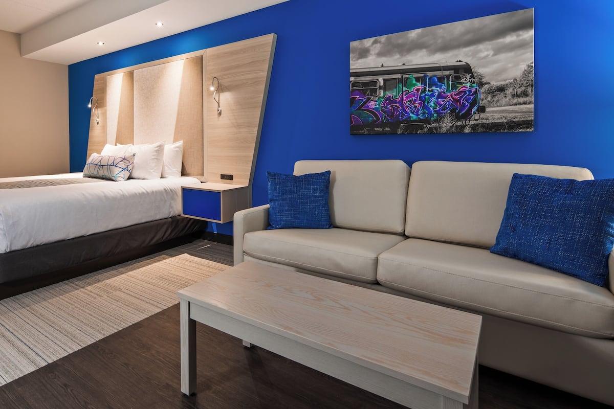 Ein modernes Hotelzimmer mit einem Bett, einer Couch, einem Couchtisch und einem Graffiti-Gemälde an der Wand.