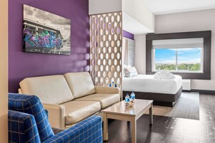 Una habitación de hotel con sofá, cama, mesa de centro y un ventanal con vistas a la ciudad.