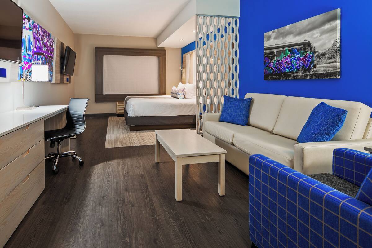 Ein modernes Hotelzimmer mit einem Holztisch, einem Bett, einer Couch und einem Fernseher.