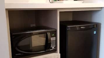 A compact kitchen with a black microwave and refrigerator, a white countertop, and a power outlet.