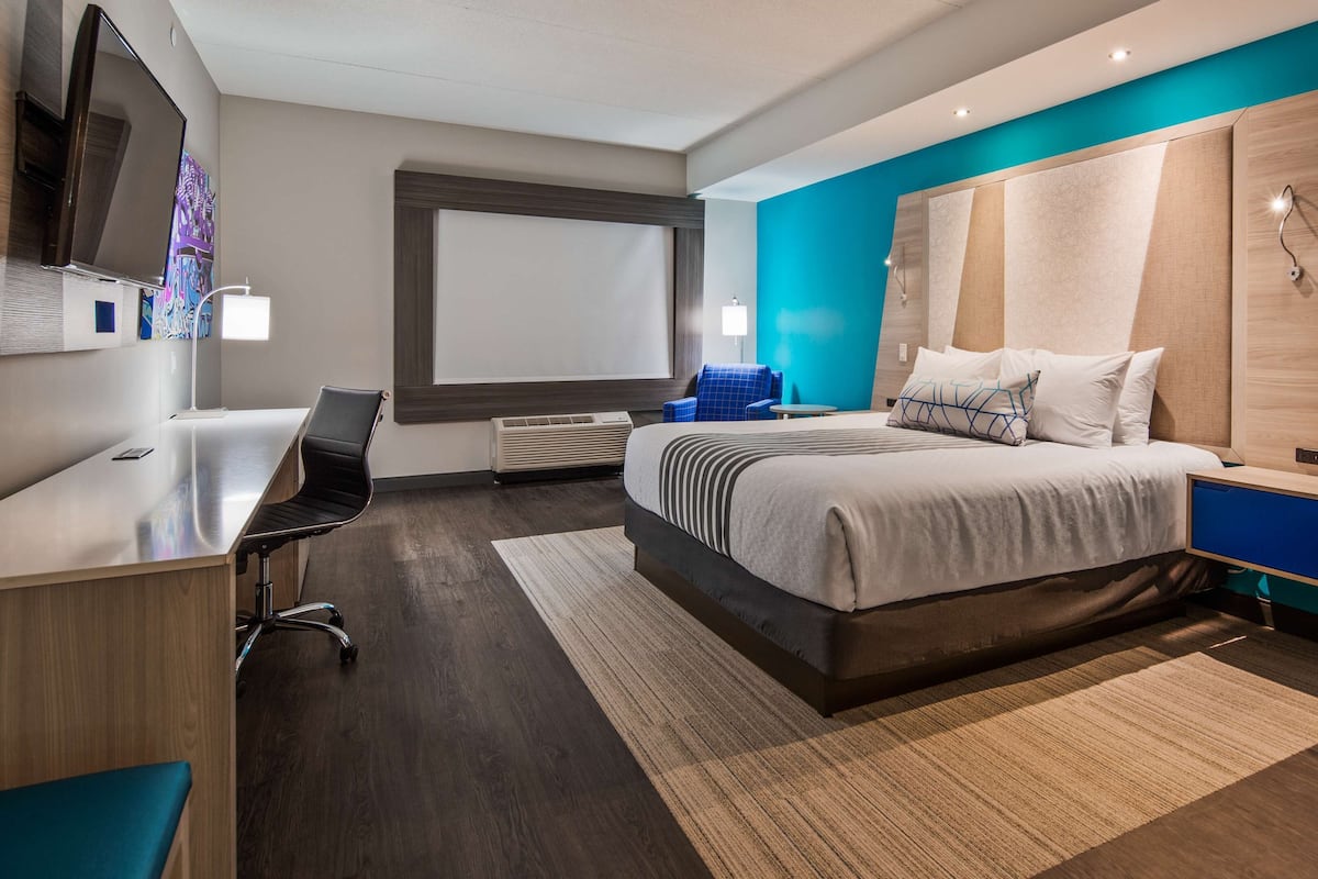 Ein modernes Hotelzimmer mit einem großen Bett, einem Schreibtisch, einem Stuhl und einem Fernseher.