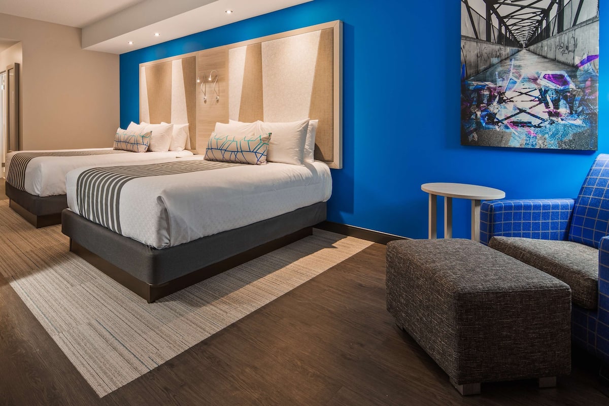 Ein Hotelzimmer mit zwei Betten, einem Schreibtisch, einem Stuhl und einem kleinen Tisch.