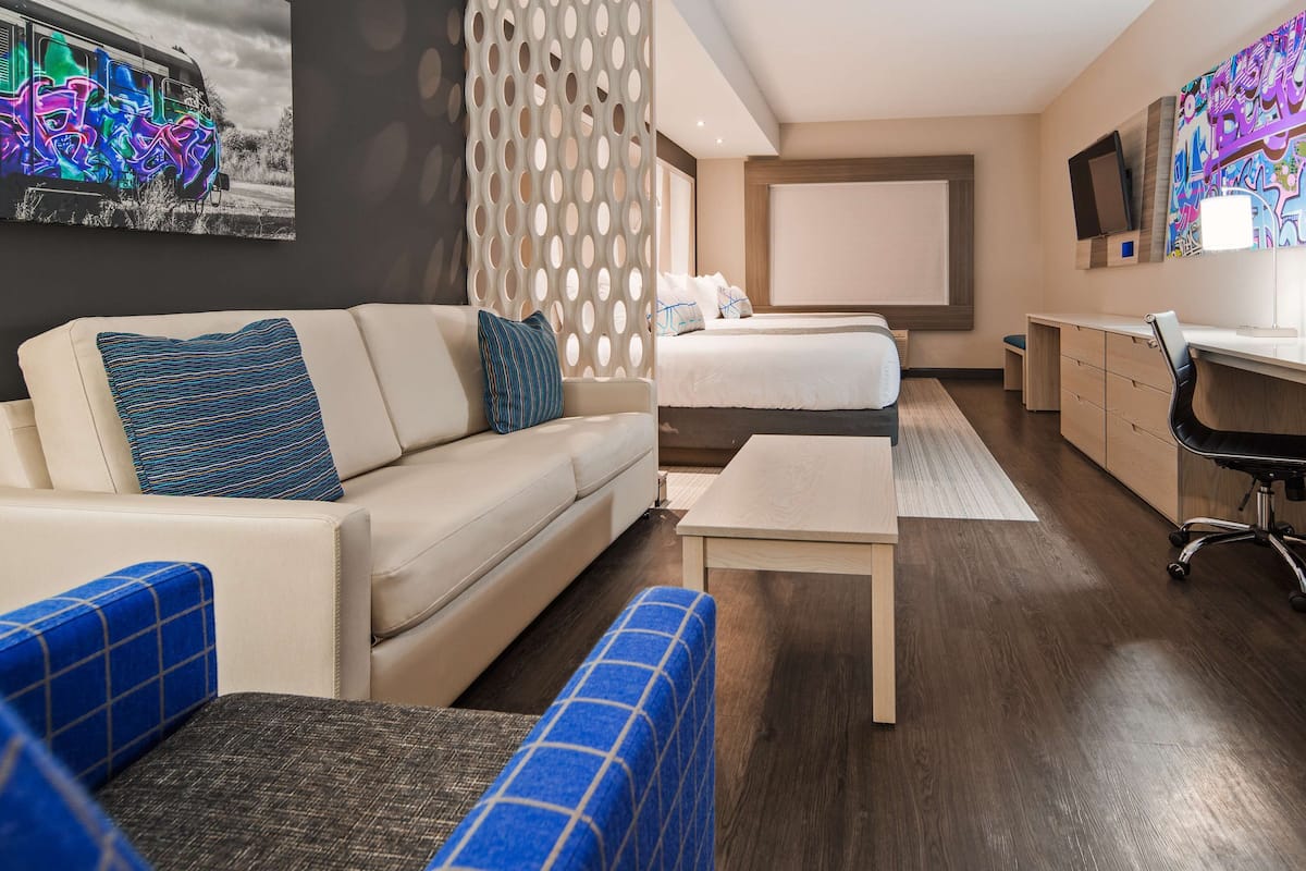 Ein modernes Hotelzimmer mit einer Couch, einem Bett, einem Schreibtisch und einem Fernseher.
