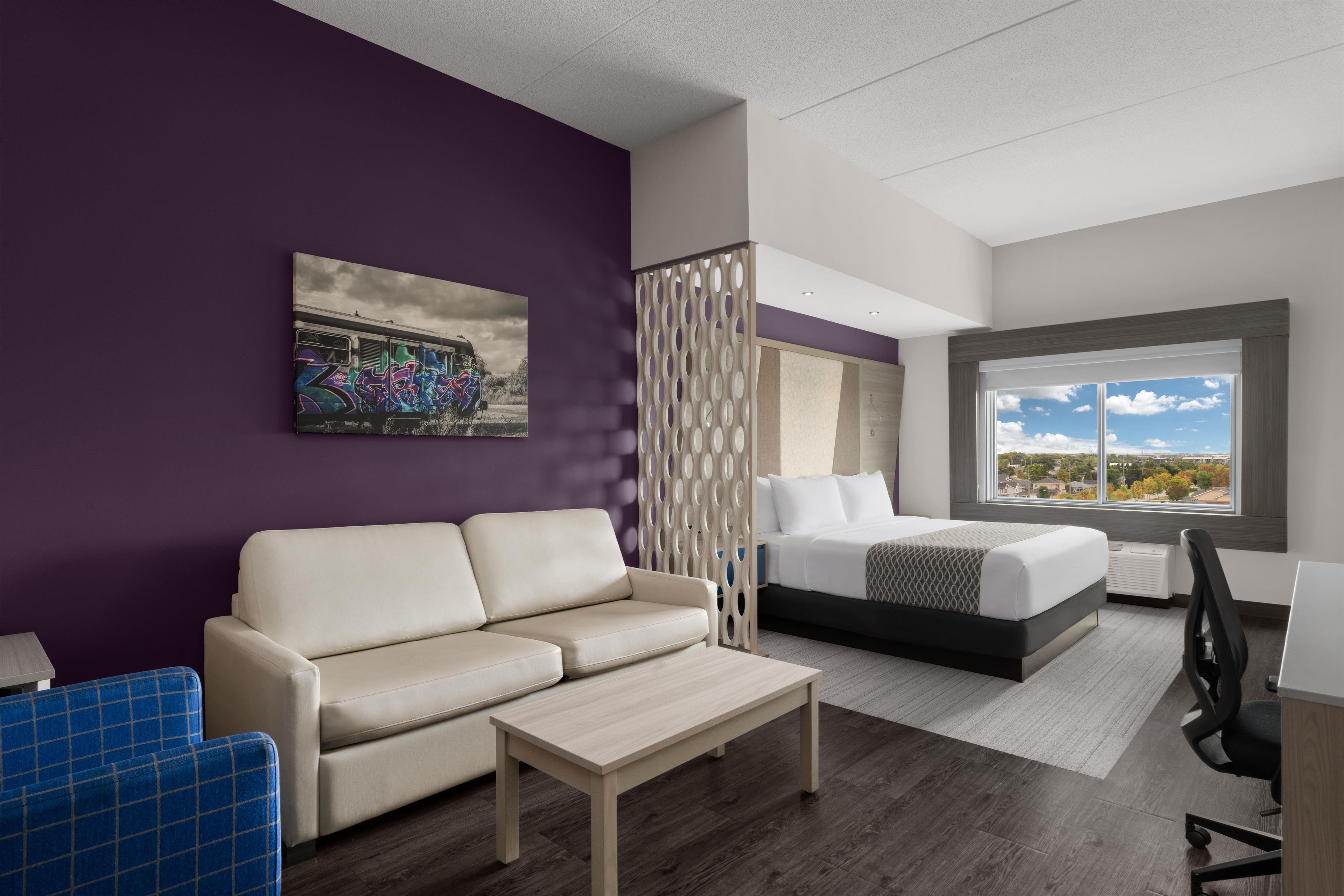 A modern hotel room with a sofa, a bed, a desk, and a large window offering a view.