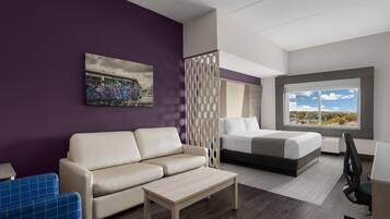 A modern hotel room with a sofa, a bed, a desk, and a large window offering a view.