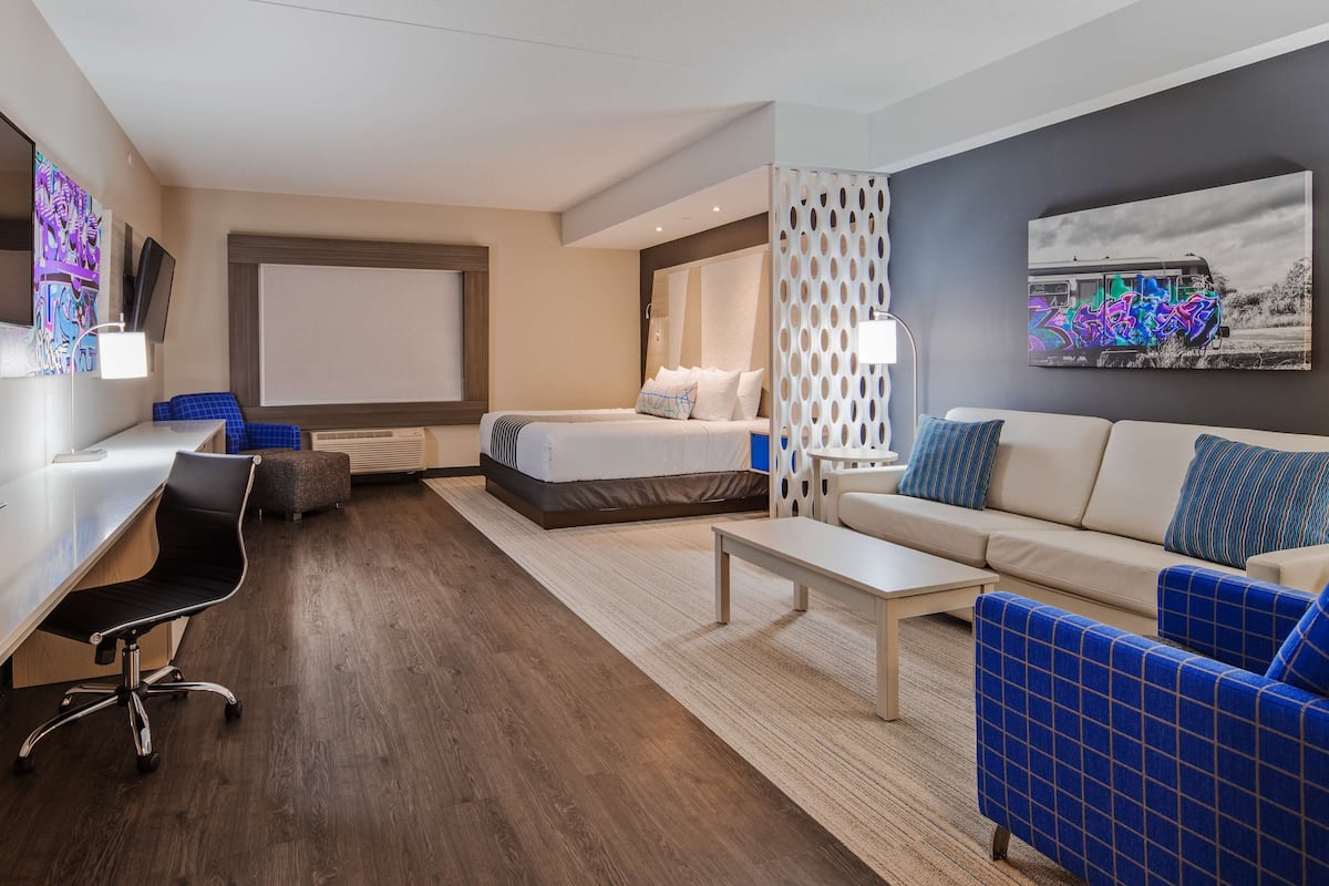 Ein modernes Hotelzimmer mit einem Bett, einem Schreibtisch, einem Sessel, einer Couch und einem Fernseher.