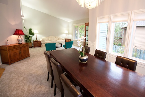 A dining area with a wooden table, chairs, and a vase with flowers. There is a sofa and a lamp in the background. - Spacious, 4BR Single-Level near Parks (Beaverton)