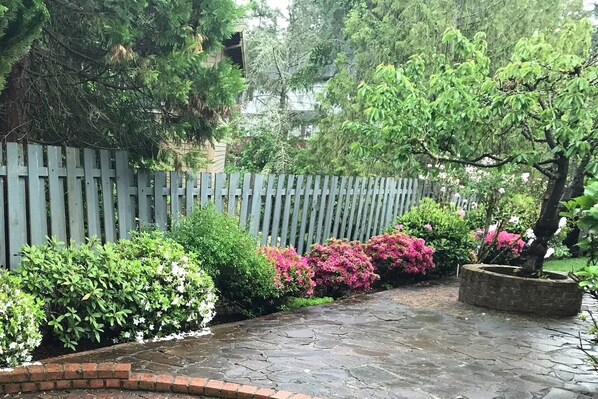 A stone pathway leading through a garden with a wooden fence, various shrubs, and flowering plants. - Spacious, 4BR Single-Level near Parks (Beaverton)