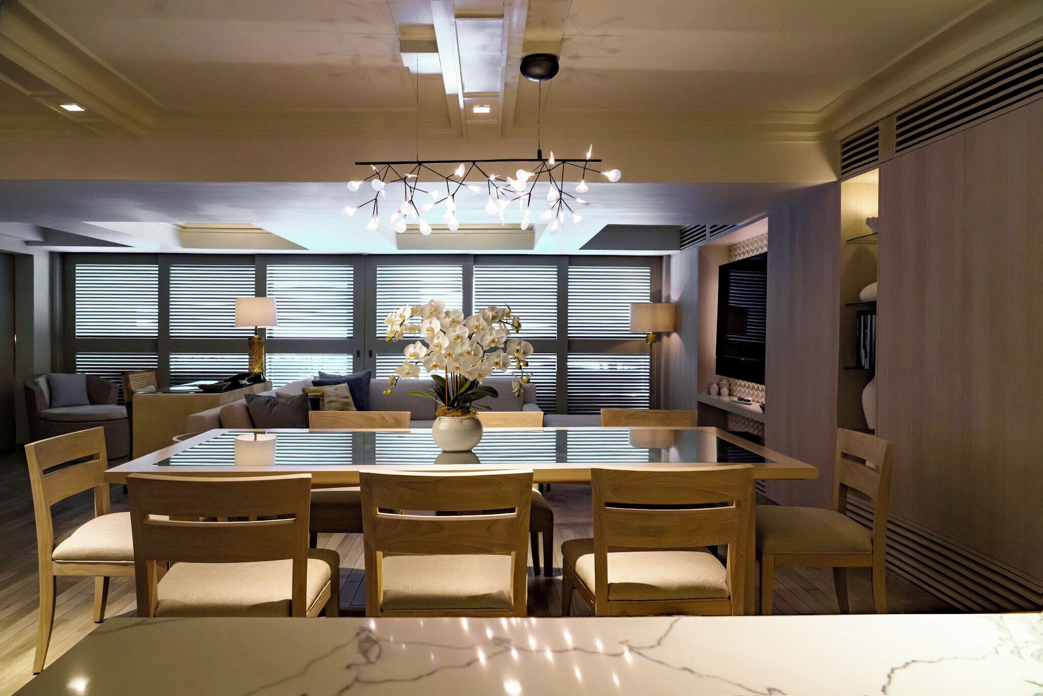 A modern dining area with a marble table, wooden chairs, and a chandelier.