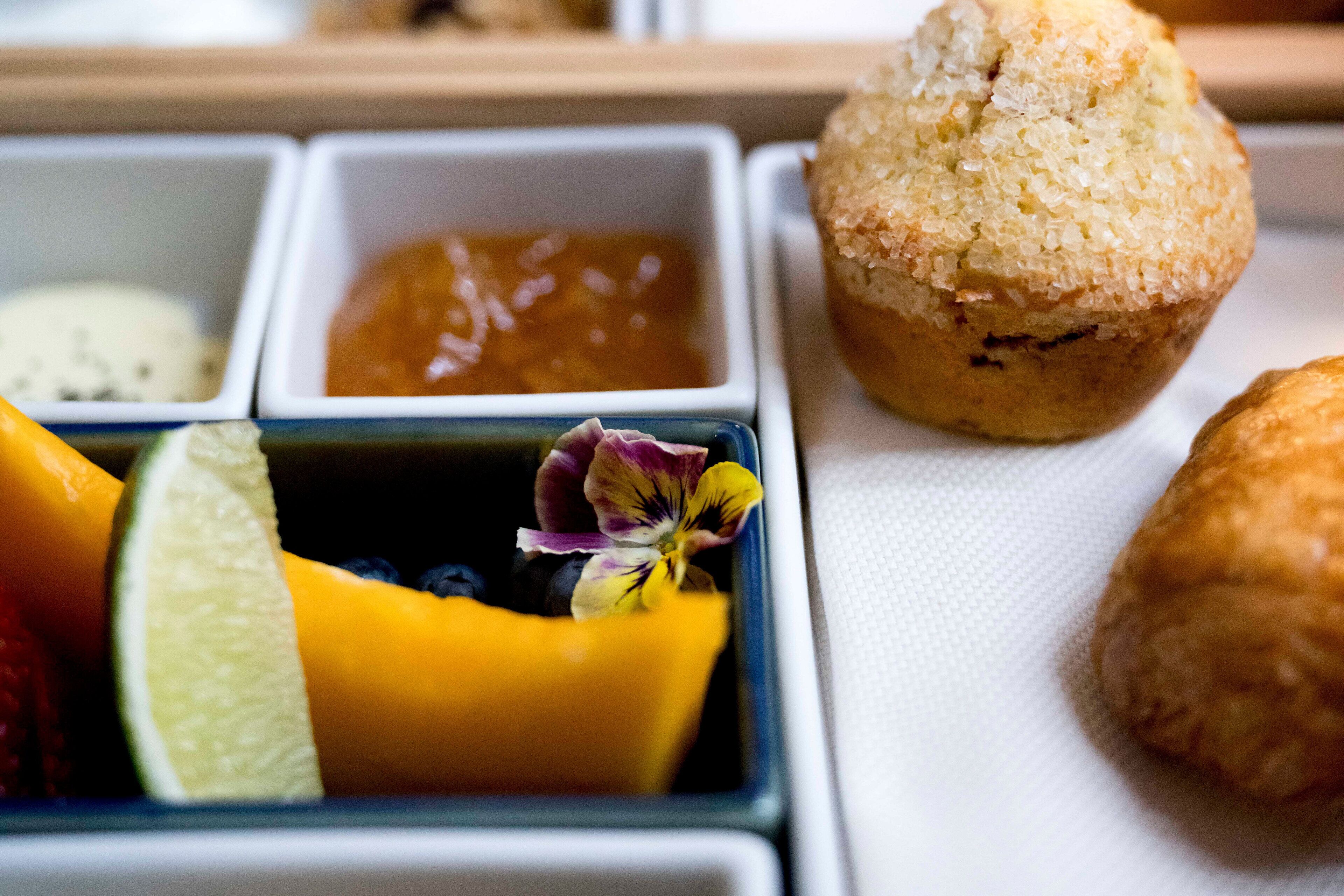 A tray with a muffin, fruit, and a small dish of jam.