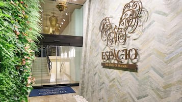 Entrada de hotel com parede verde, placa de metal decorativa e tapete azul.