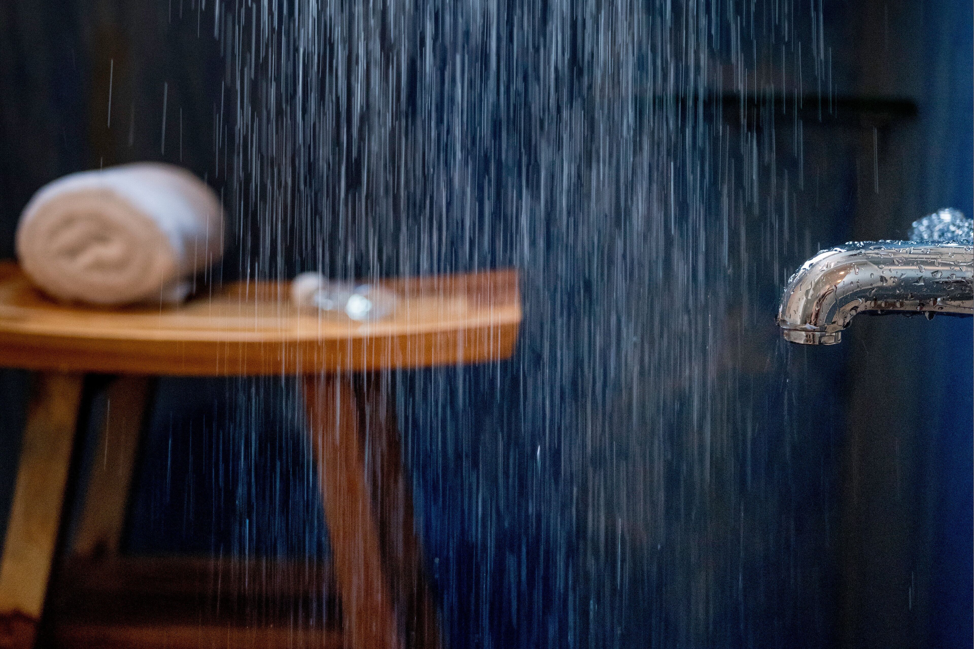 Een douche met stromend water, een handdoek op een klein houten krukje en een metalen kraan.