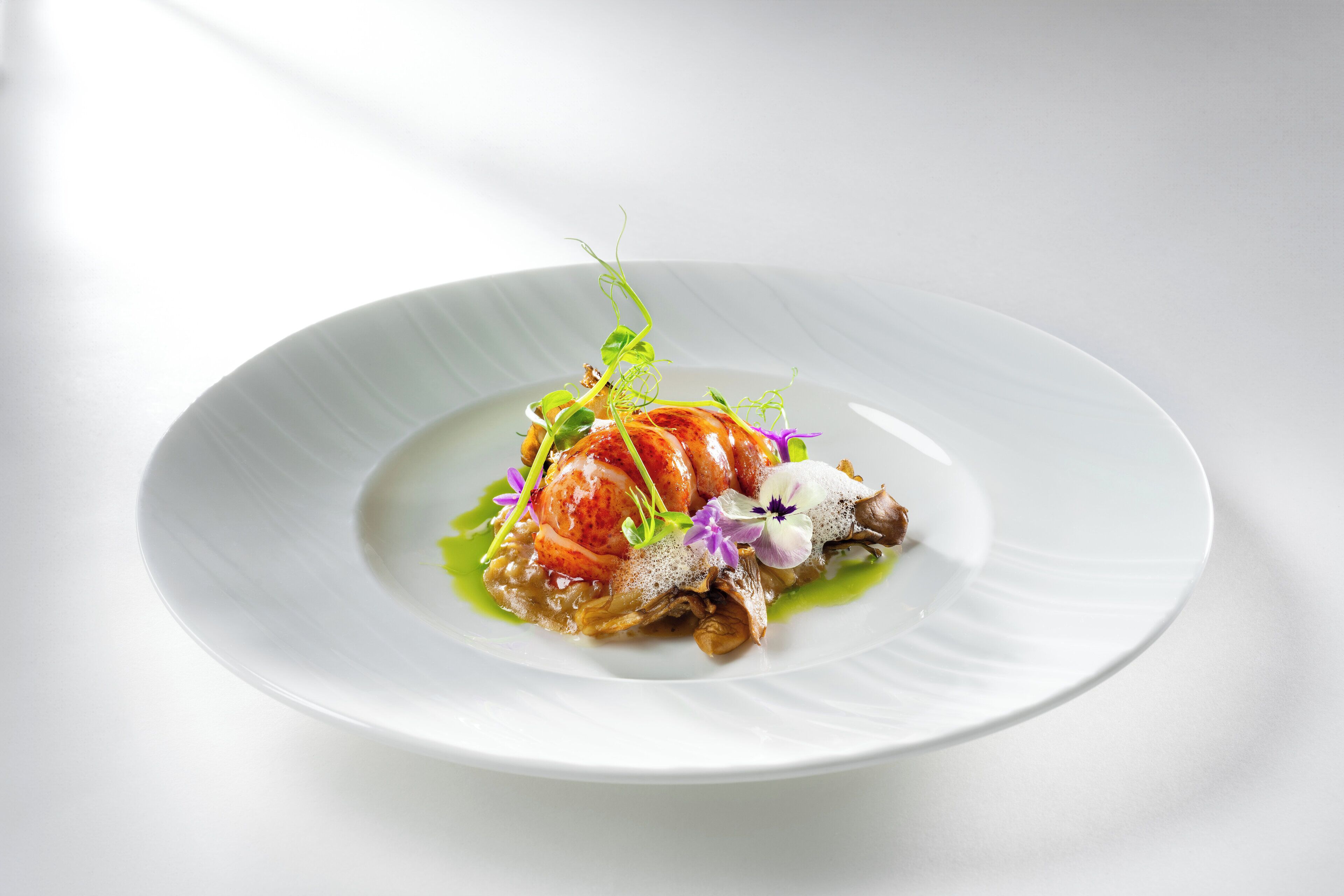 Un plato blanco con un guiso de mariscos, decorado con hojas verdes y flores moradas.
