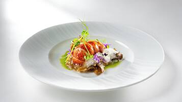 Un plato blanco con un guiso de mariscos, decorado con hojas verdes y flores moradas.