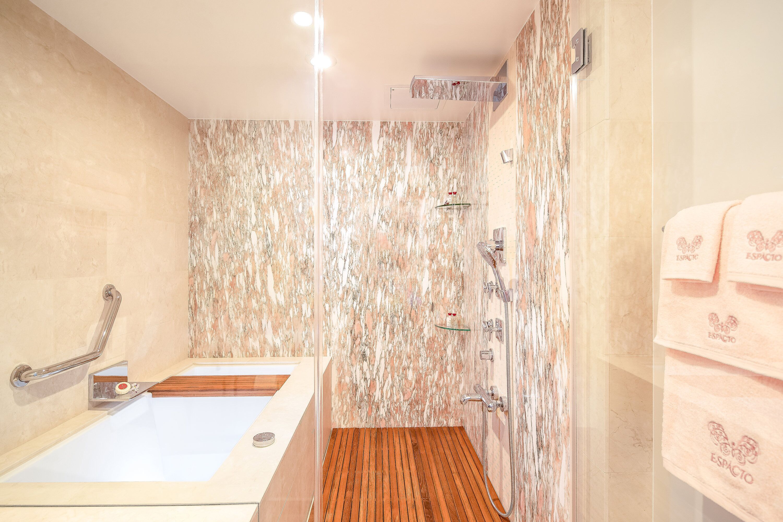 A bathroom with a marble wall, a wooden floor, a bathtub, and a shower area.