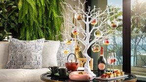 Un comedor con un centro de mesa de árbol blanco, una botella de vino y una bandeja con comida y bebidas.
