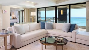 Una sala moderna con un sofá seccional color beige, una mesa de centro de vidrio y vista al océano a través de grandes puertas corredizas.