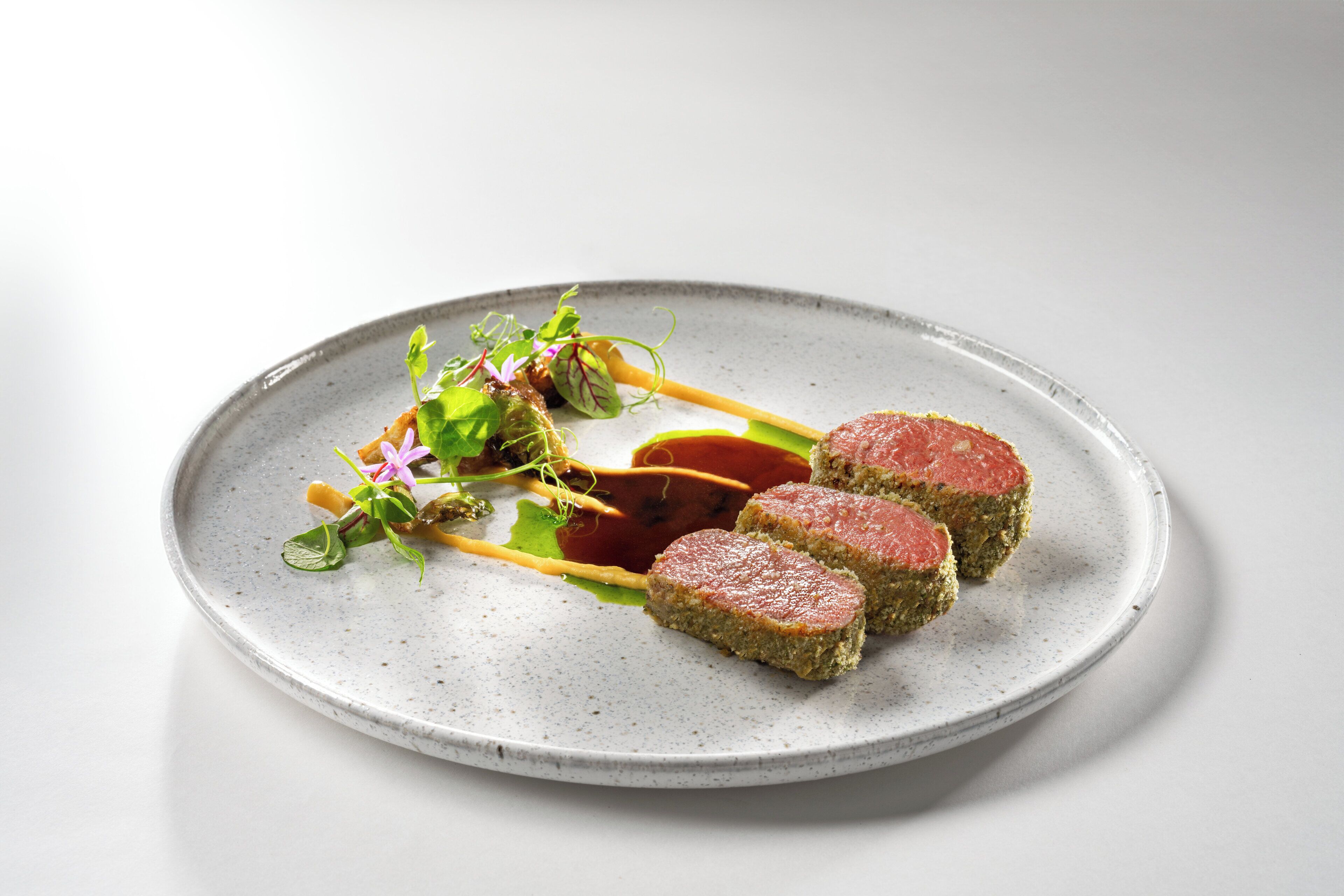 A plate with three pieces of meat, a sauce, and some greens.