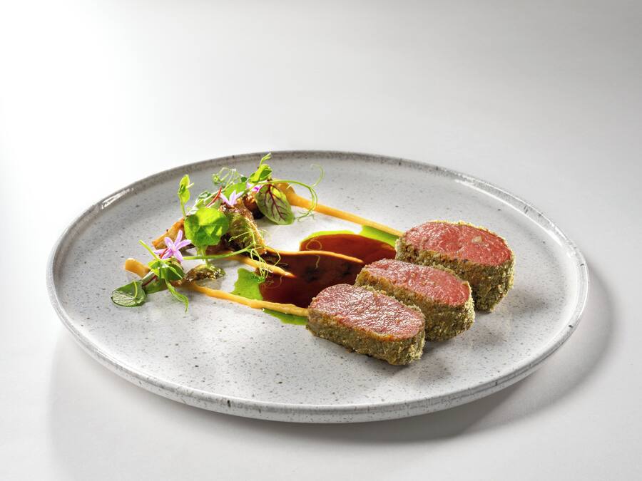 A plate with three pieces of meat, a sauce, and some greens.