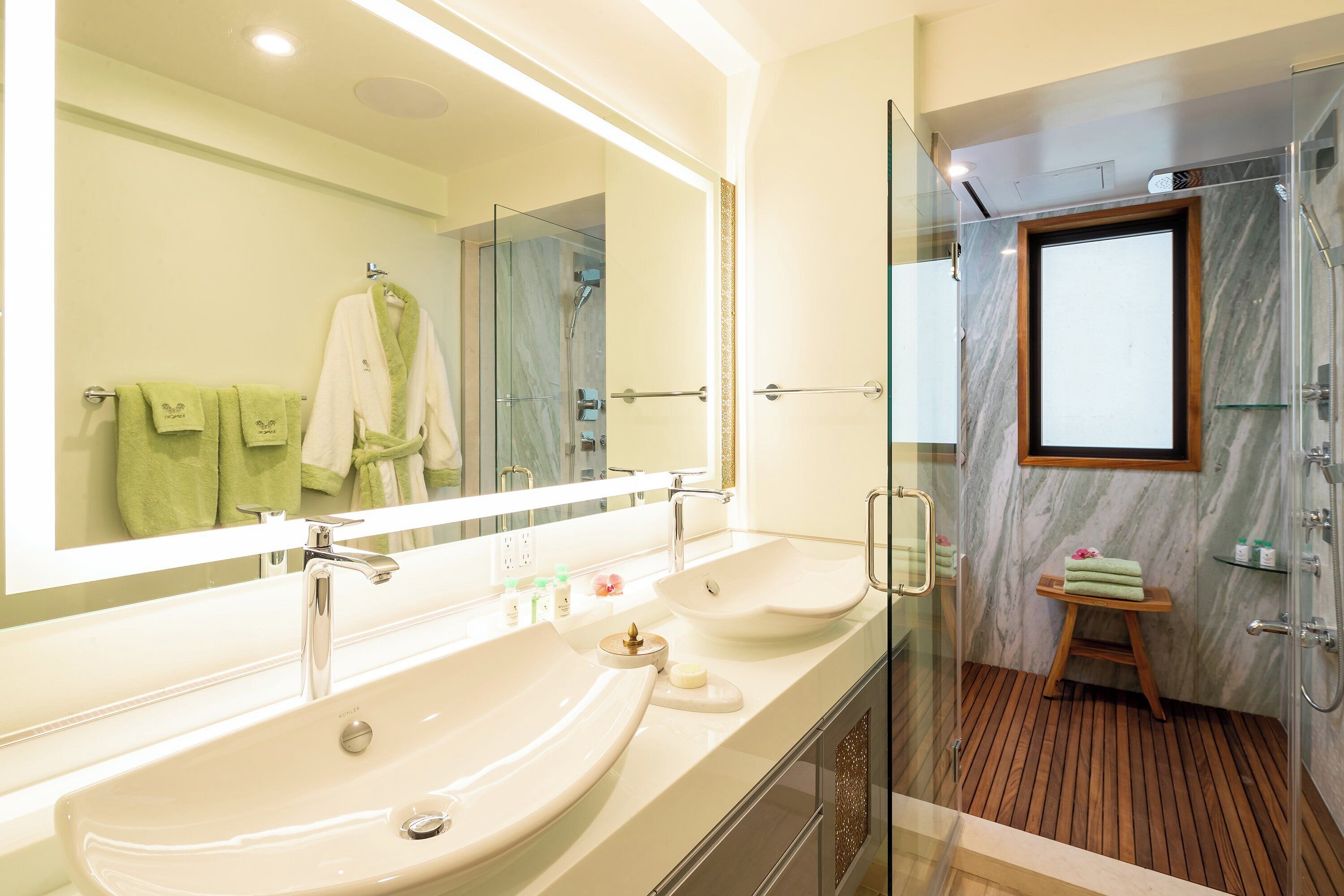 Un baño con un espejo grande, dos lavamanos, zona de ducha y un taburete de madera.