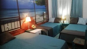 A room with two beds, a nightstand with a lamp, a window with curtains, and a view of the sea. - Habitacions Can Pau Guest House (Llanca)