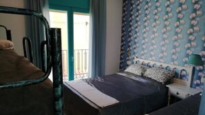 A bedroom with two beds, a window with curtains, a patterned wall, and a nightstand with a lamp. - Habitacions Can Pau Guest House (Llanca)