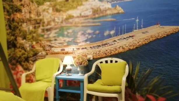 A room with a beach view mural, two chairs, a small table with a lamp, and a plant. - Habitacions Can Pau Guest House (Llanca)
