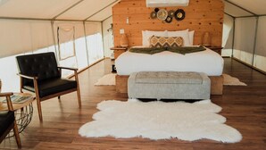 Ein Zeltraum mit einem Bett, einem Sessel, einem Teppich und Holzwänden.