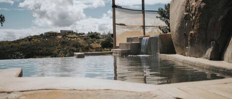 Ein Pool mit Wasserfall, Steintreppe und einem großen Felsen.