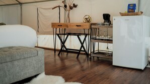 Ein Zeltraum mit einem Bett, einem Schreibtisch mit Computer, einem Kühlschrank und einer Kaffeemaschine.