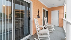 A covered porch with white rocking chairs, a sliding glass door, and a white door. - Peachtree Place By Panhandle Getaways (Panama City Beach)