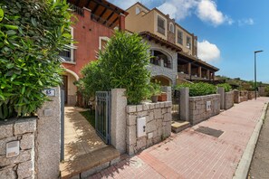 A residential street with stone walls, a gated entrance, and a clear sky. - Holiday Home "Raggio di Luna" with Wi-Fi, Air Conditioning, Balcony & Garden (Villasimius)