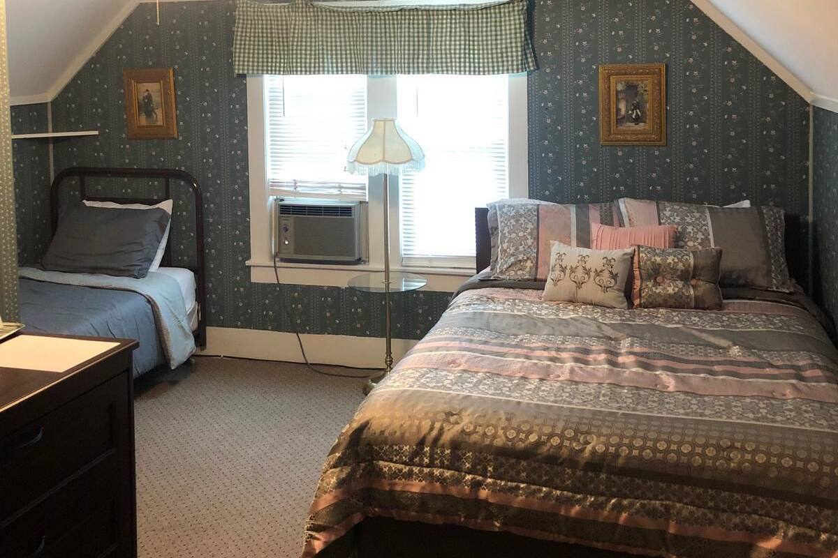 A bedroom with two beds, a window with blinds, a lamp, and a dresser.