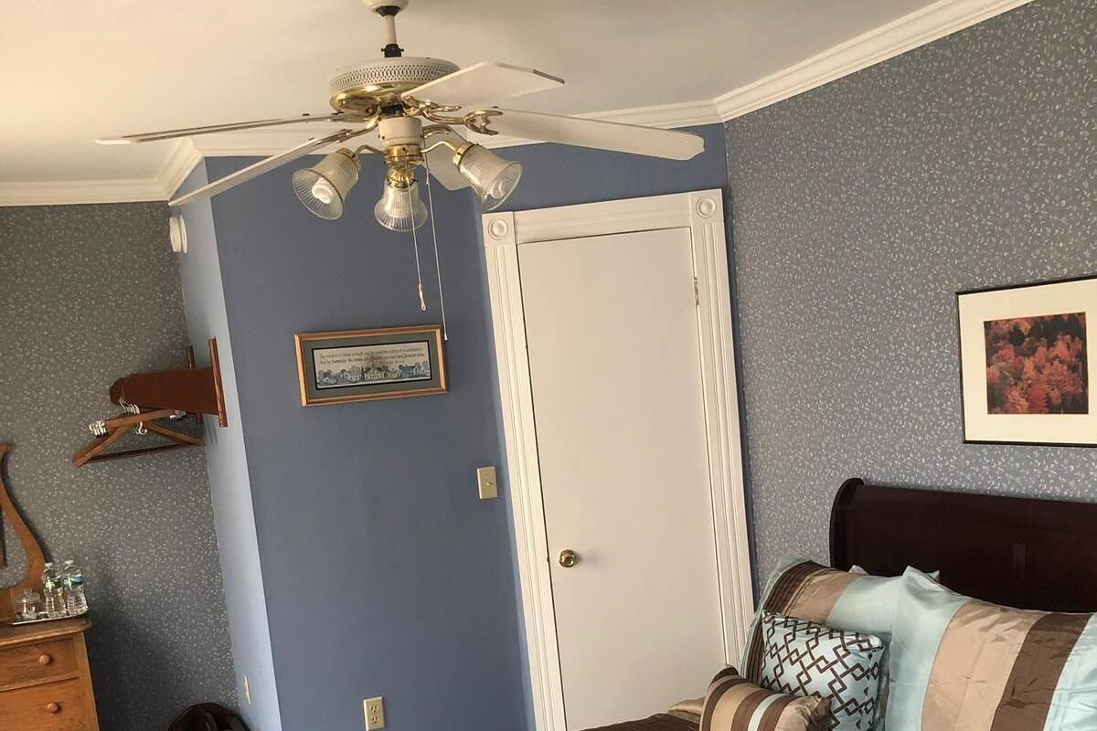 A bedroom with a bed, a dresser, a ceiling fan, and a door.