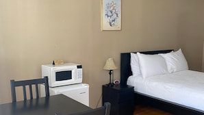 A bedroom with a bed, bedside table, lamp, and a microwave on a small table.