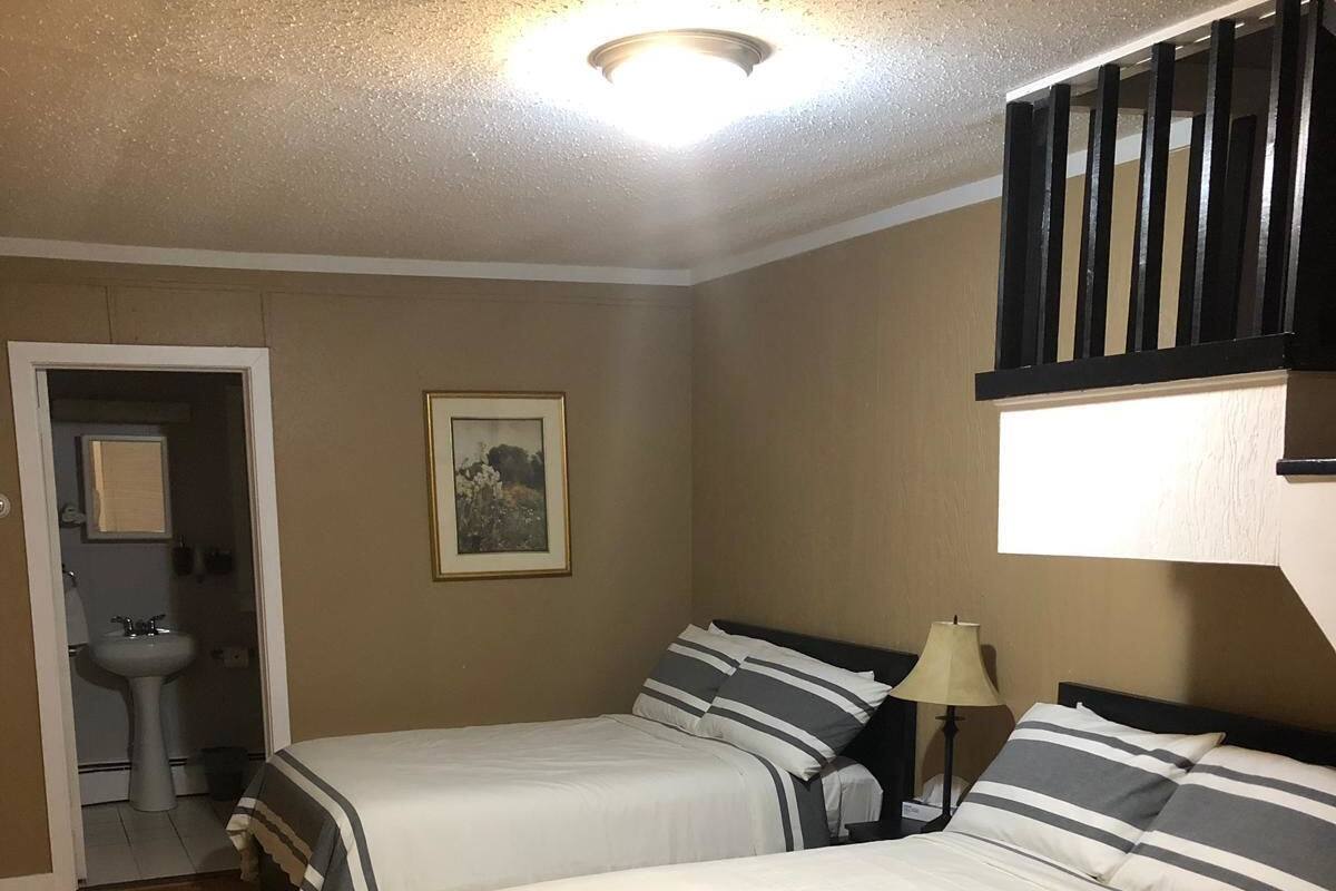 A room with two beds, a desk, a chair, a lamp, and a painting on the wall.