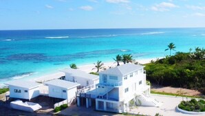 A beachfront property with a multi-story building, a covered patio, and a view of the ocean. - Mika's Resort (Governor's Harbour)