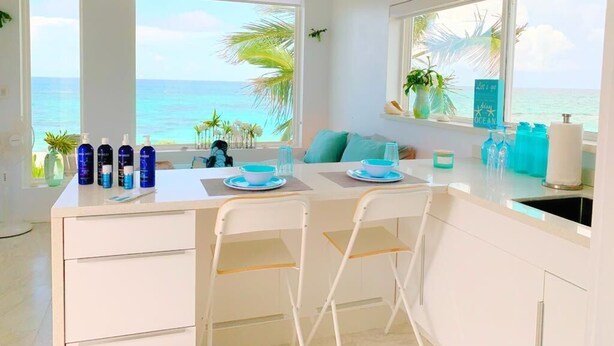 A bright kitchen with large windows overlooking the ocean, a white countertop, and bar stools. - Mika's Resort (Governor's Harbour)
