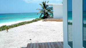 A wooden deck leading to a beach with a palm tree and a small building. - Mika's Resort (Governor's Harbour)