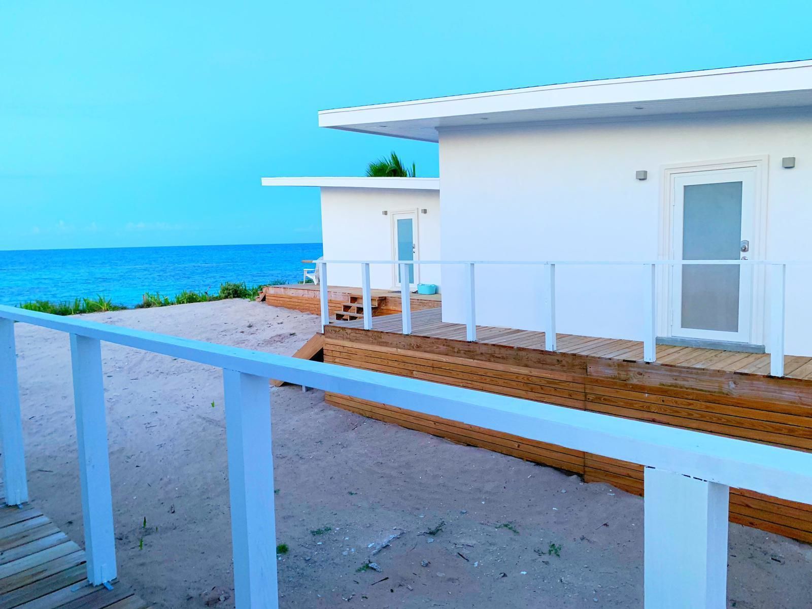 Un edificio frente a la playa con una terraza de madera y barandilla blanca, con vista al océano.
