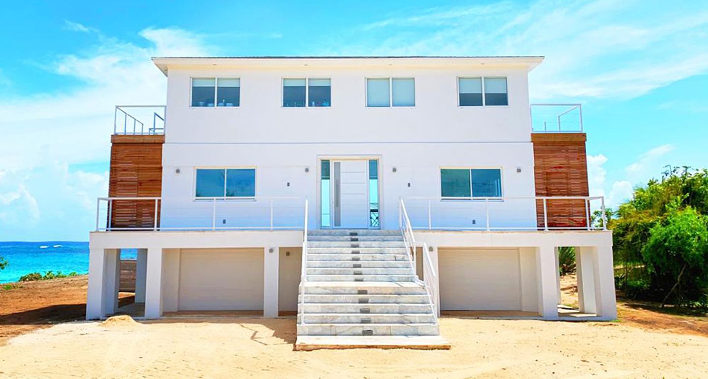 Ein modernes Strandhaus mit zwei Etagen, einer Treppe zum Eingang, einer Garage und Blick auf den Ozean.