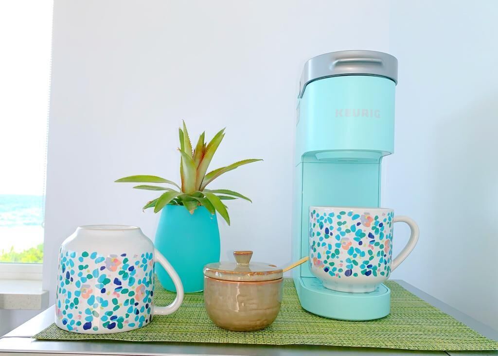 A coffee maker, two cups, a teapot, and a plant on a table.