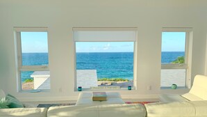 A living room with a view of the ocean through three windows. - Mika's Resort (Governor's Harbour)