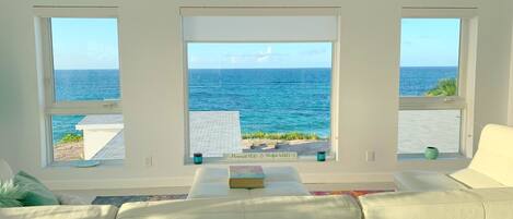 A living room with a view of the ocean through three windows.