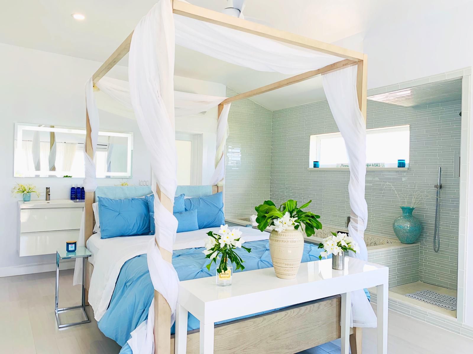 A modern bedroom with a four-poster bed, a vanity with a mirror, and a shower area.