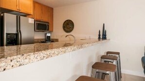 Una cocina moderna con encimeras de granito, electrodomésticos de acero inoxidable, armarios de madera y una barra con taburetes.